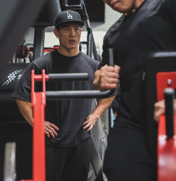 Kevin Bae watching a client train on a gym machine.
